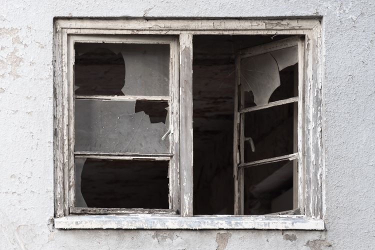 Image of broken window, cement house, gray and white with broken glass. 