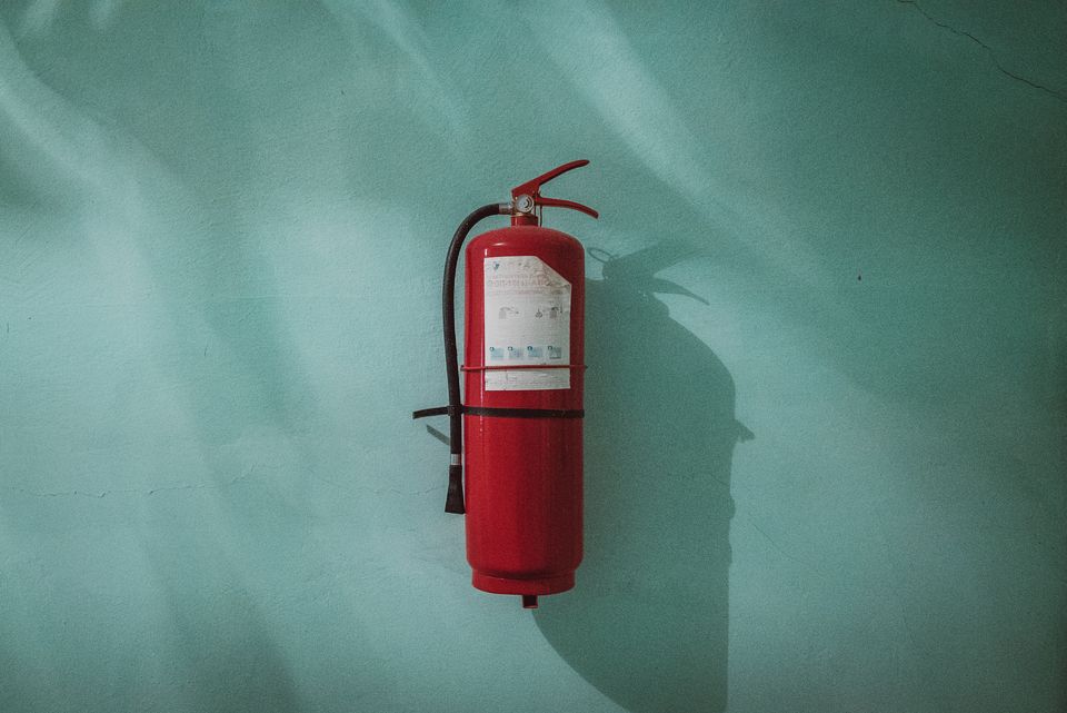 Red metal fire extinguisher on green pastel wall. 