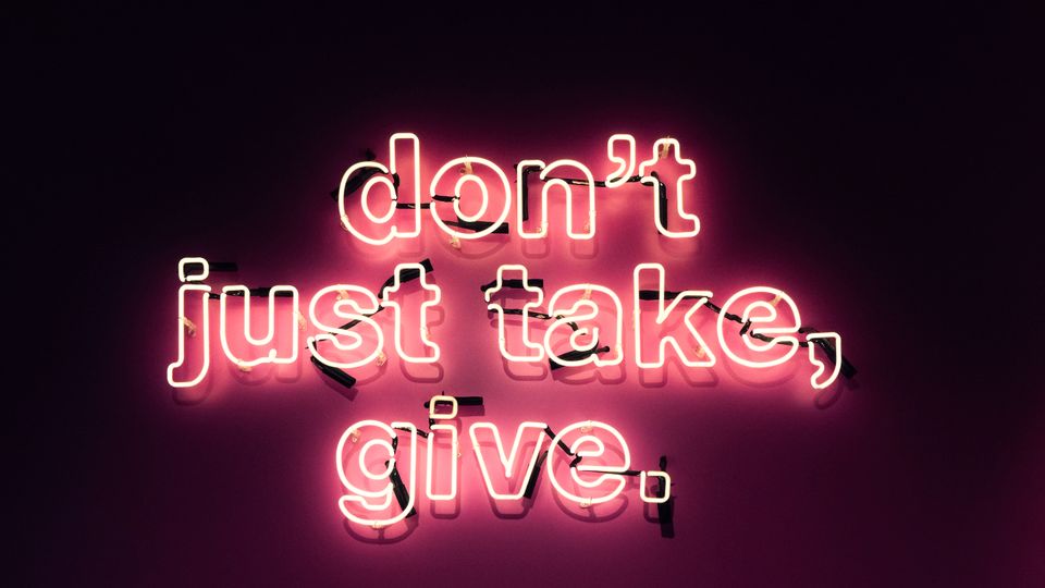 Image of wall with pink neon sign. All lowercase "don't just take, give."