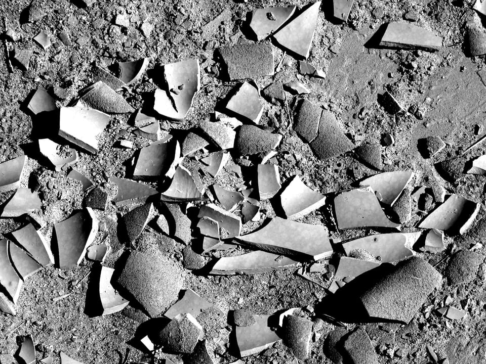 Broken pottery on dirt; photograph all in gray.