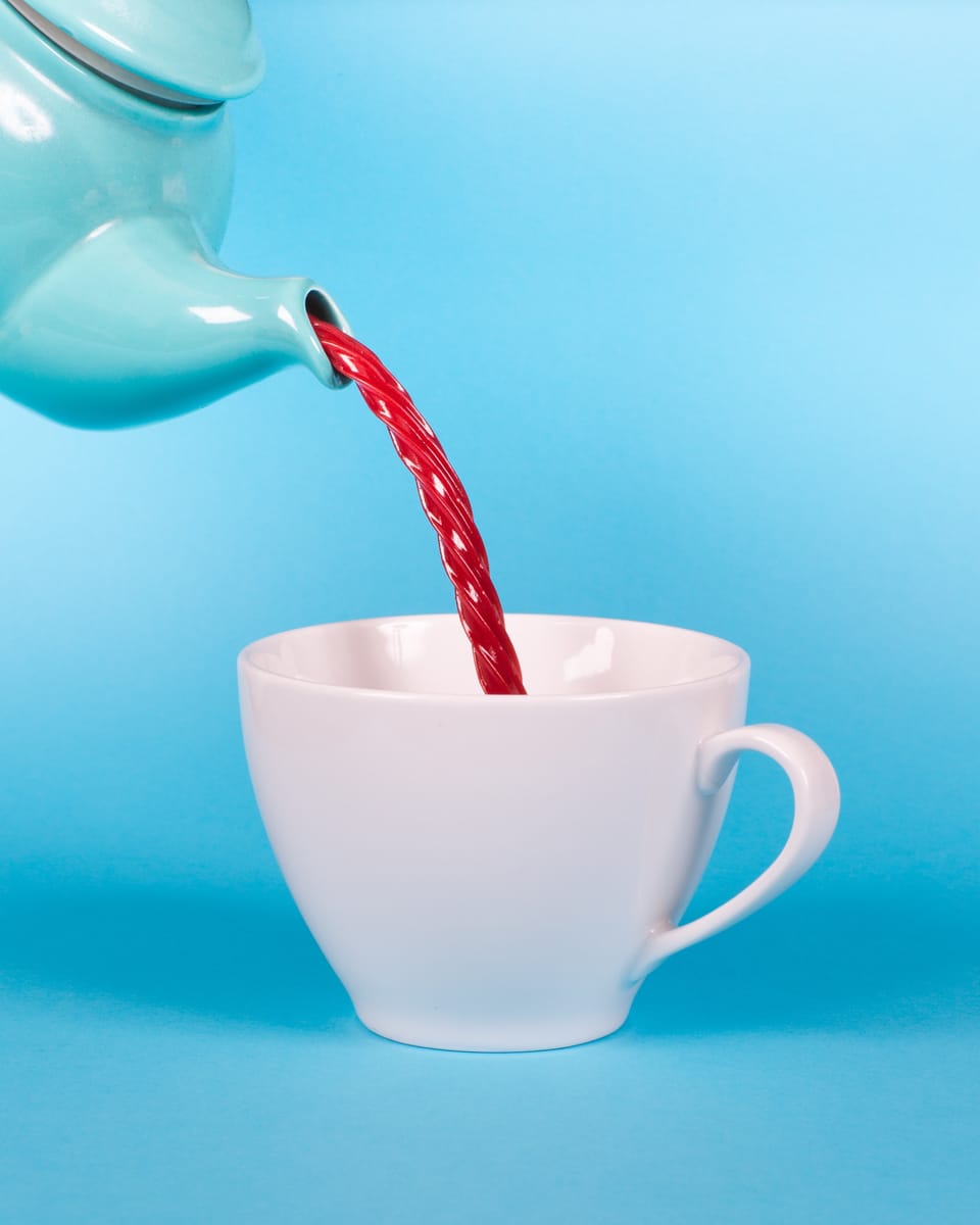 Tea pot on blue background pouring red licorice into a white tea cup.